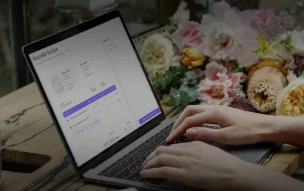 Professionnelle utilisant MyUnisoft sur ordinateur portable pour gérer son activité commerciale et sa facturation électronique dans une boutique de fleurs